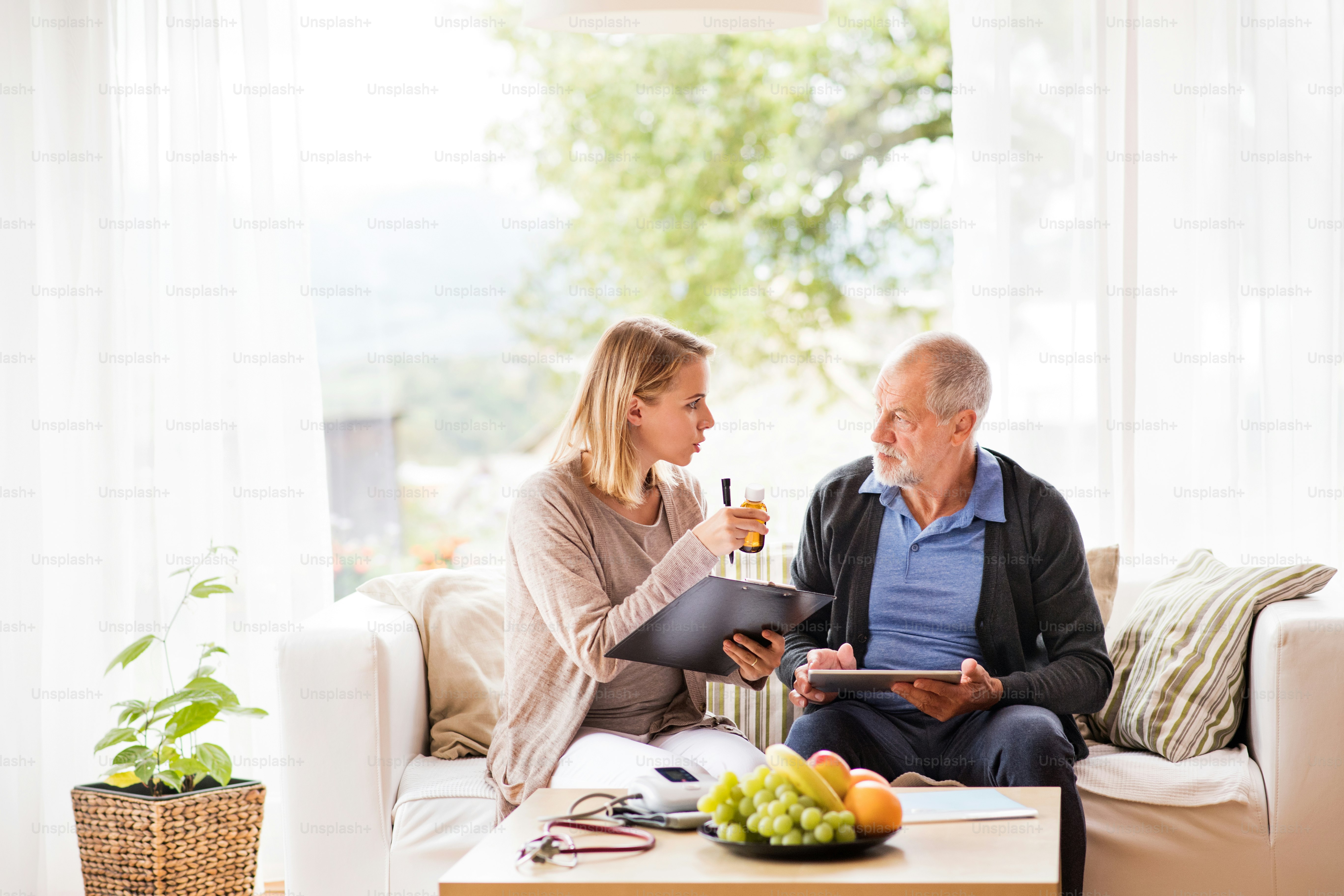 Health visitor and a senior man during home visit. A female nurse or a doctor showing test results on a tablet